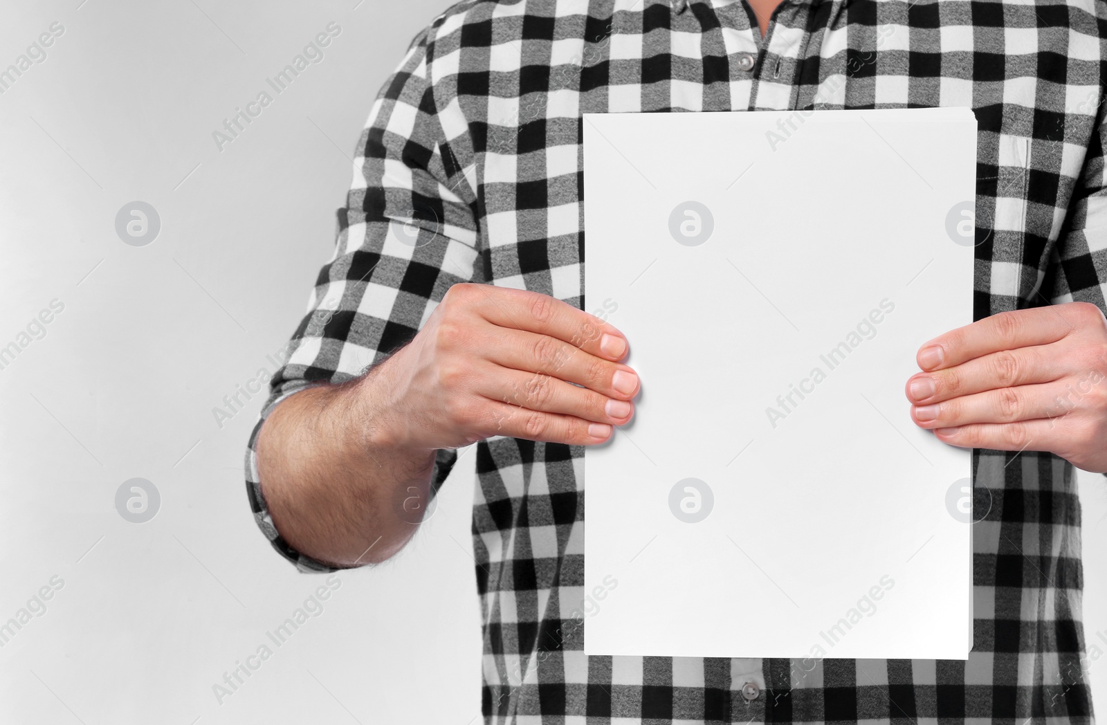 Photo of Man holding sheet of paper on light grey background, closeup. Mockup for design