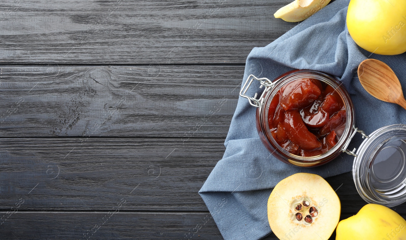 Photo of Quince jam in glass jar, spoon and fresh raw fruits on grey wooden table, flat lay. Space for text