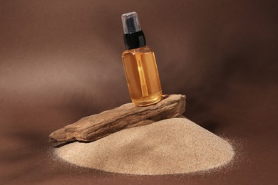 Bottle of serum and tree bark on sand against brown background