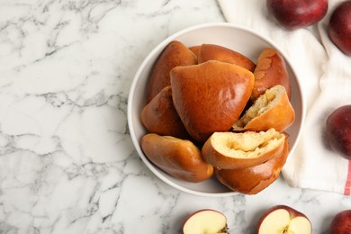 Delicious baked apple pirozhki in bowl and fruits on white marble table, flat lay. Space for text