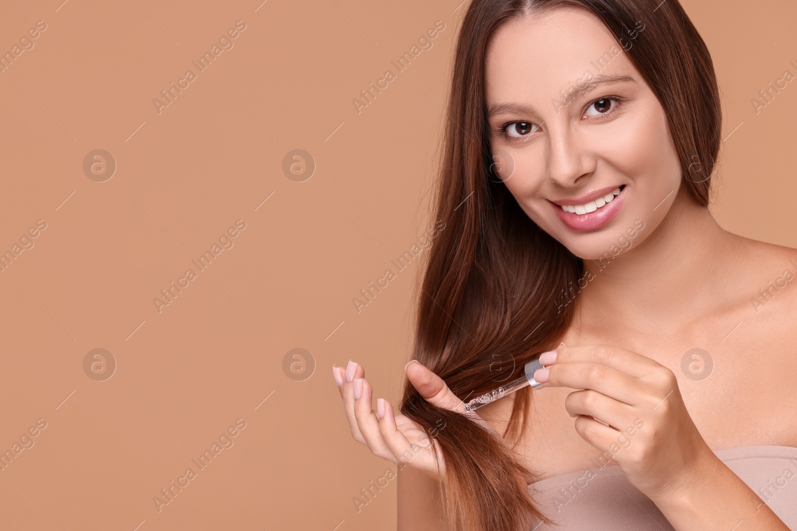 Photo of Beautiful woman applying serum onto hair on beige background, space for text