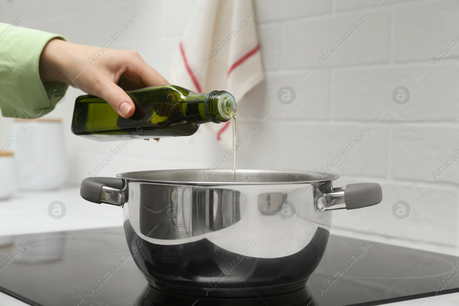 Photo of Woman pouring cooking oil from bottle into pot in kitchen, closeup