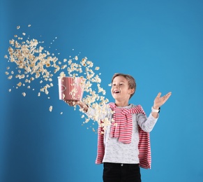 Cute boy scattering popcorn from bucket on color background