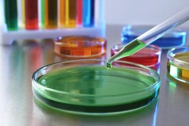 Photo of Dripping green liquid into Petri dish on grey table in laboratory, closeup