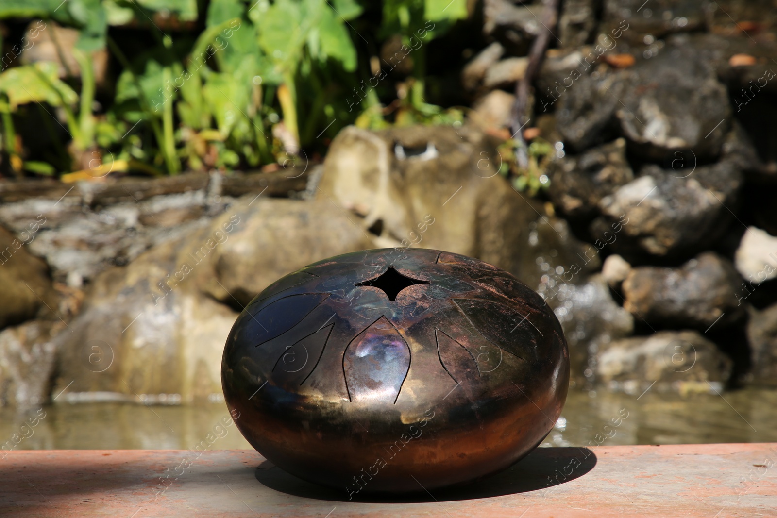 Photo of Steel tongue drum near pond on sunny day. Percussion musical instrument