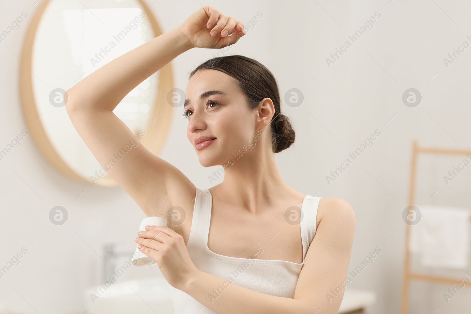 Photo of Beautiful young woman applying deodorant in bathroom