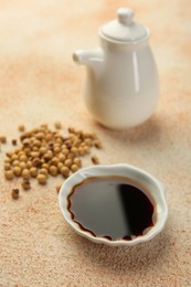 Photo of Soy sauce in bowl and beans on beige textured table