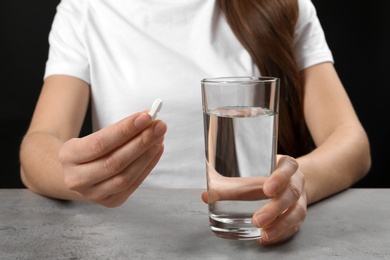 Photo of Woman holding pill and glass of water at table, closeup