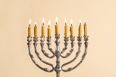 Photo of Silver menorah with burning candles on beige background. Hanukkah celebration