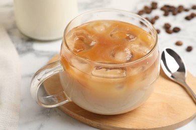 Photo of Refreshing iced coffee with milk in glass cup and spoon on white table, closeup