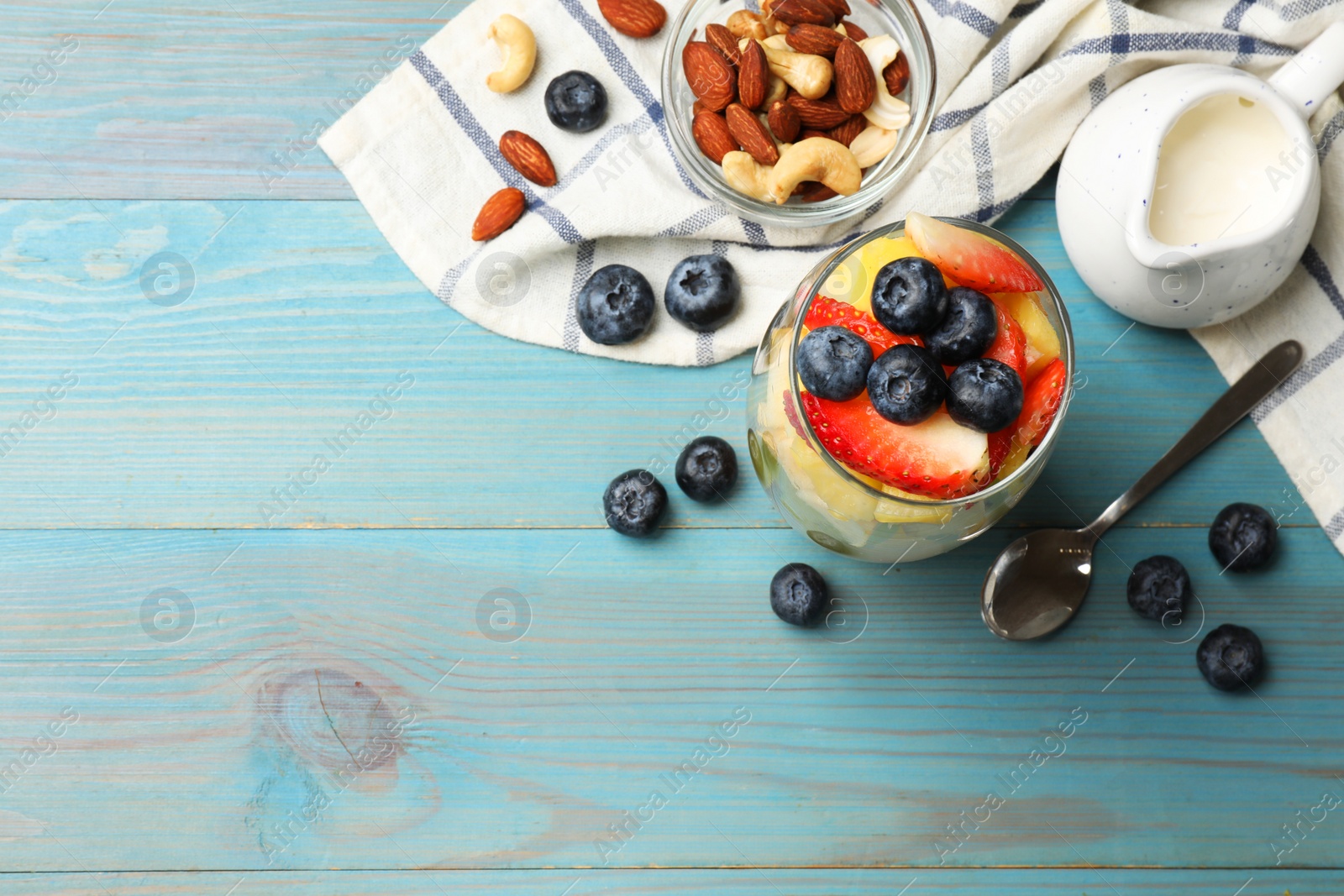 Photo of Delicious fruit salad, fresh berries and nuts on light blue wooden table, flat lay. Space for text