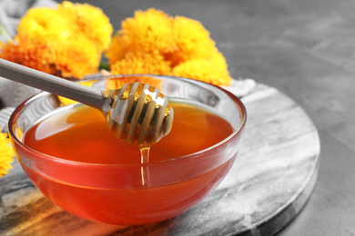 Photo of Glass bowl with organic honey and dipper on board, closeup