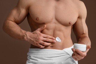 Man applying moisturizing cream onto his body on brown background, closeup