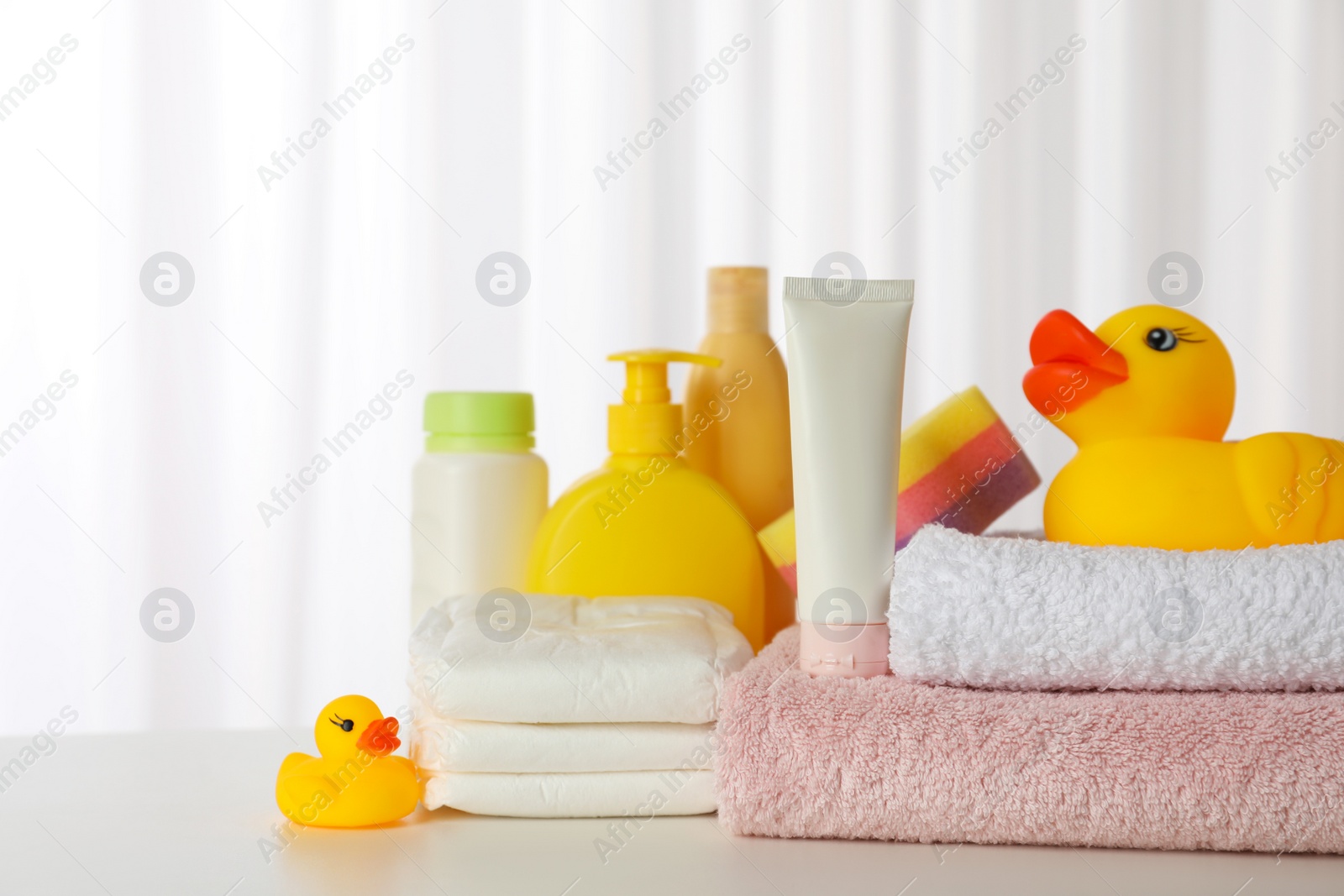 Photo of Towels, rubber ducks and baby care products on white table indoors