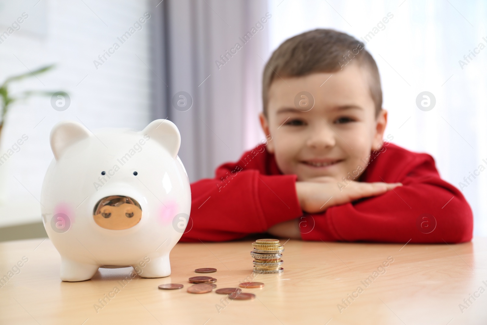 Photo of Little boy with piggy bank and money at home, closeup