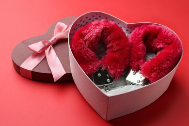 Photo of Gift box with furry handcuffs on red background