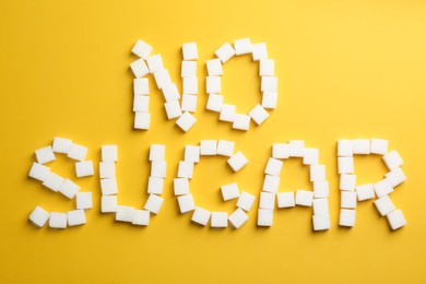 Photo of Phrase No Sugar made of refined cubes on yellow background, flat lay