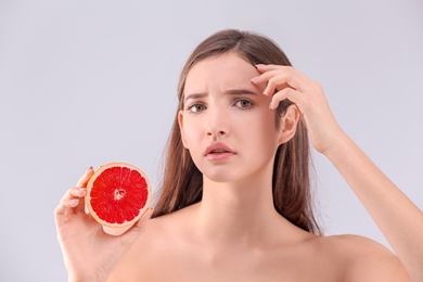 Teenage girl with acne problem holding grapefruit against grey background