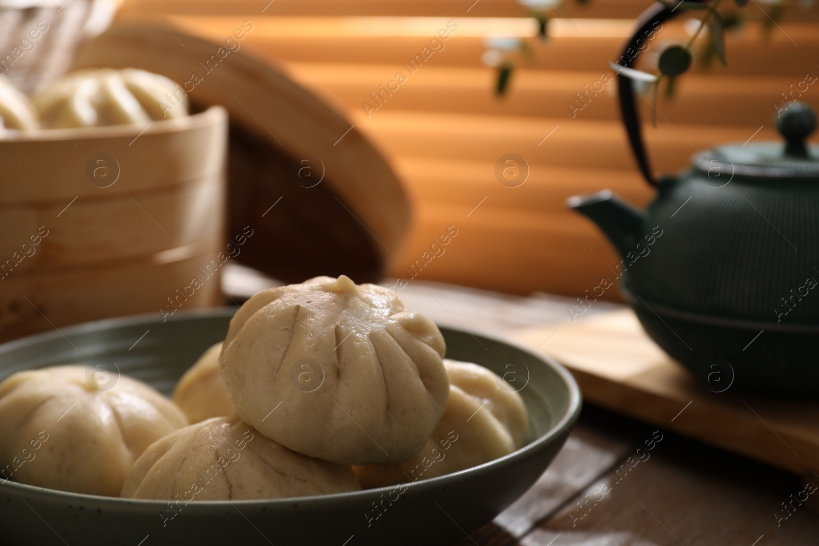 Photo of Delicious bao buns (baozi) in bowl on wooden table, closeup