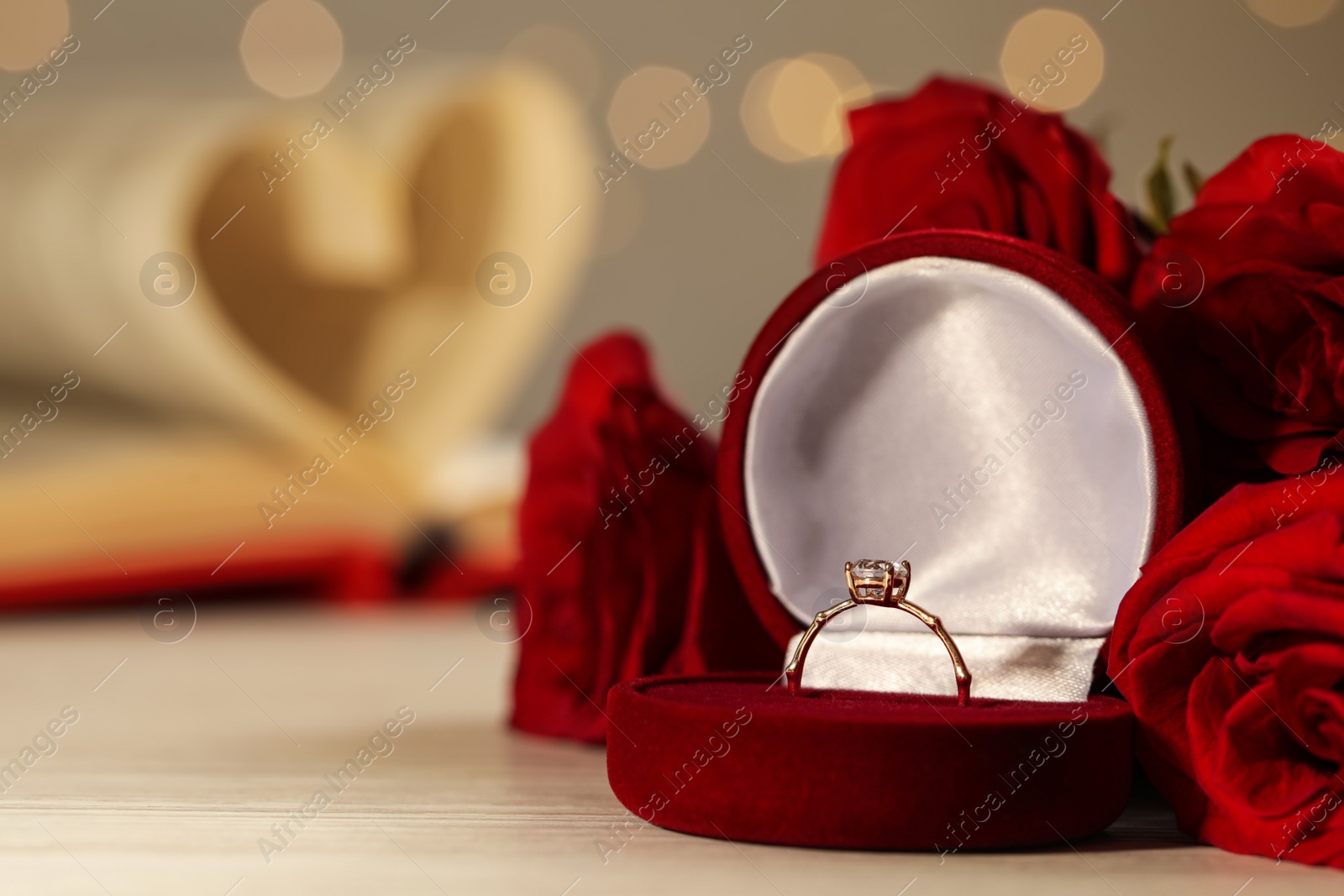 Photo of Beautiful engagement ring with gemstone in box and flowers on white wooden table. Space for text