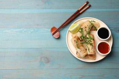 Photo of Tasty fried spring rolls served on light blue wooden table, flat lay. Space for text