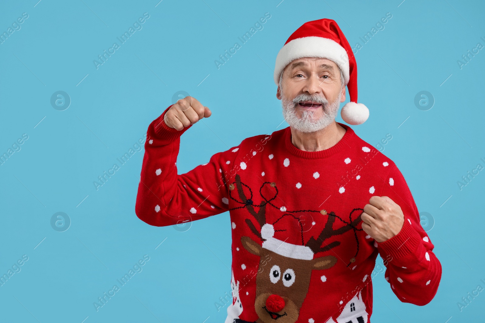 Photo of Senior man in Christmas sweater and Santa hat on light blue background. Space for text