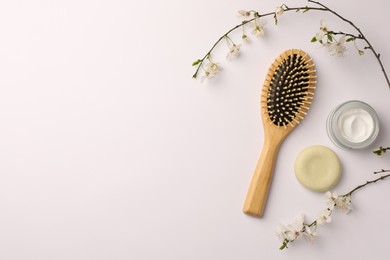 Photo of Wooden hairbrush, cosmetic products and branch with flowers on white background, flat lay. Space for text