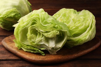 Board with halves of fresh green iceberg lettuce head on wooden table, closeup