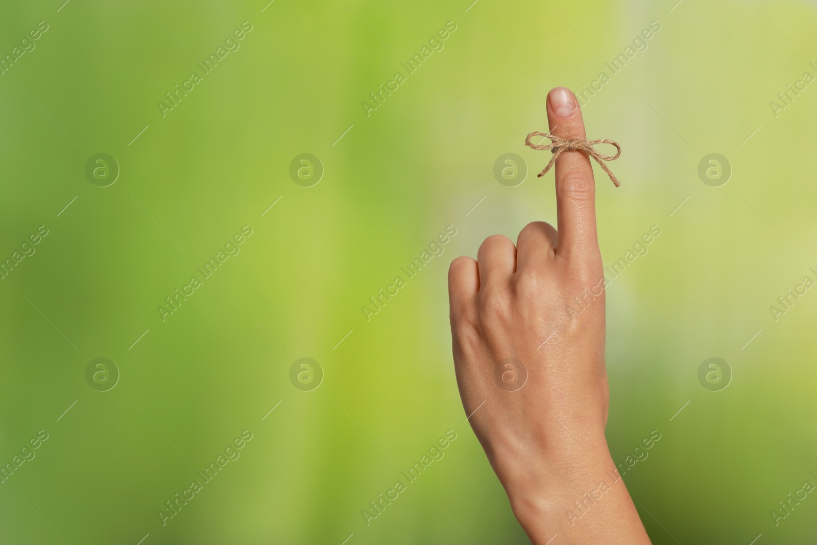 Photo of Woman showing index finger with tied bow as reminder on green blurred background, closeup. Space for text