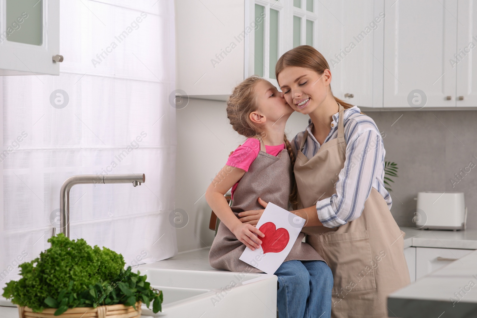 Photo of Little daughter congratulating mom with greeting card in kitchen. Happy Mother's Day