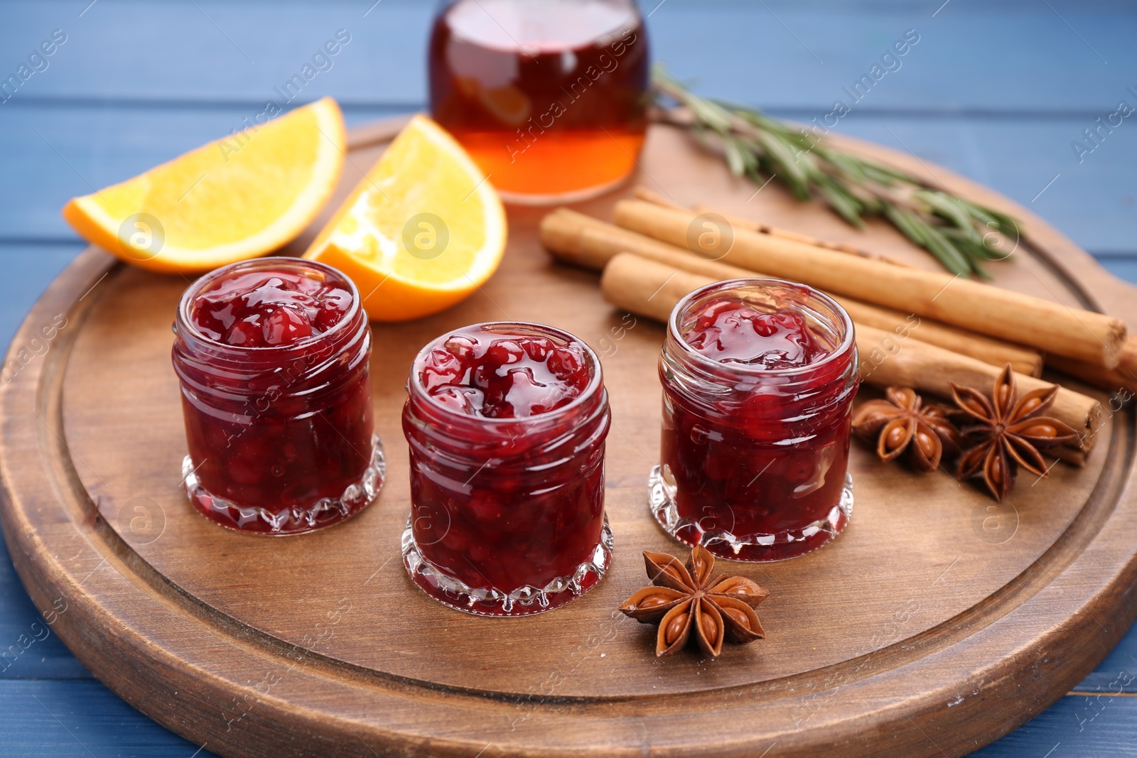 Photo of Cranberry sauce in jars and ingredients on blue wooden table, closeup