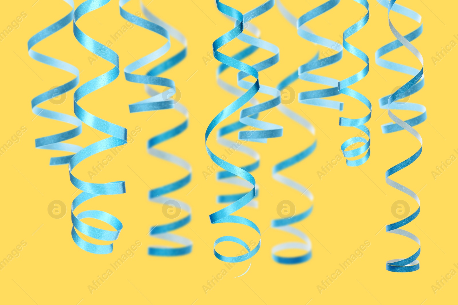 Image of Many light blue serpentine streamers on yellow background. Party decor