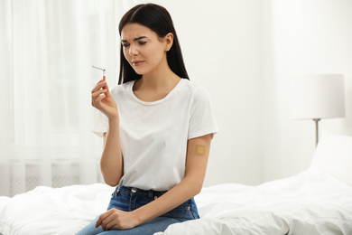Photo of Emotional young woman with nicotine patch and cigarette in bedroom