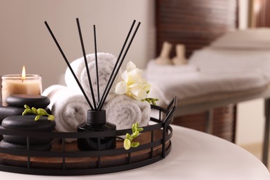 Photo of Aromatic reed air freshener, rolled towels, spa stones and candle on white table indoors