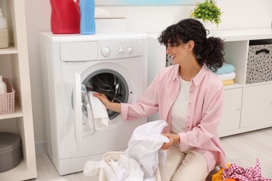 Happy woman putting laundry into washing machine indoors