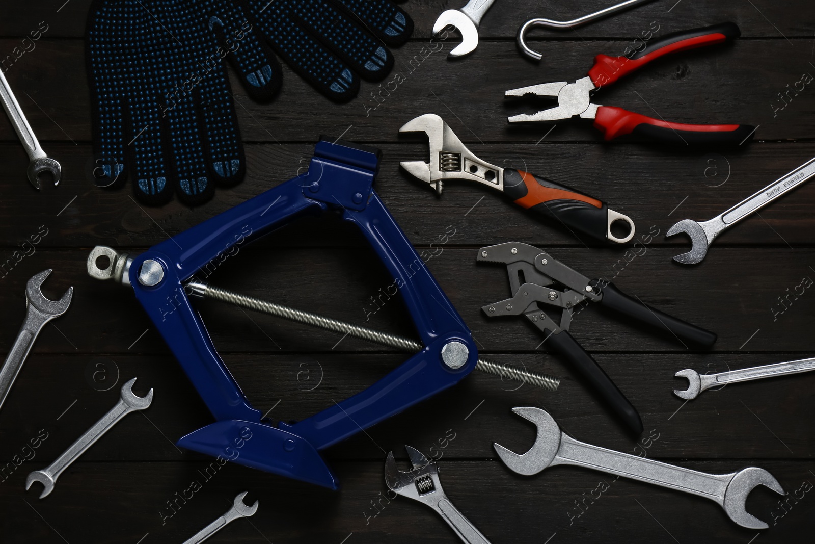 Photo of Car scissor jack, gloves and different tools on black wooden surface, flat lay