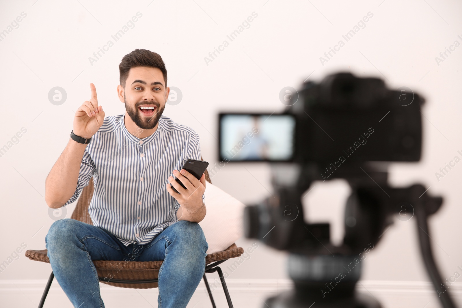 Photo of Young blogger with smartphone recording video on camera indoors