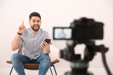 Photo of Young blogger with smartphone recording video on camera indoors
