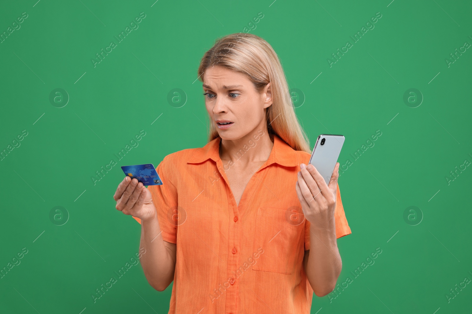 Photo of Stressed woman with credit card and smartphone on green background. Be careful - fraud