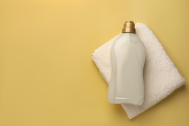 Photo of Bottle of fabric softener and terry towel on pale yellow background, top view. Space for text