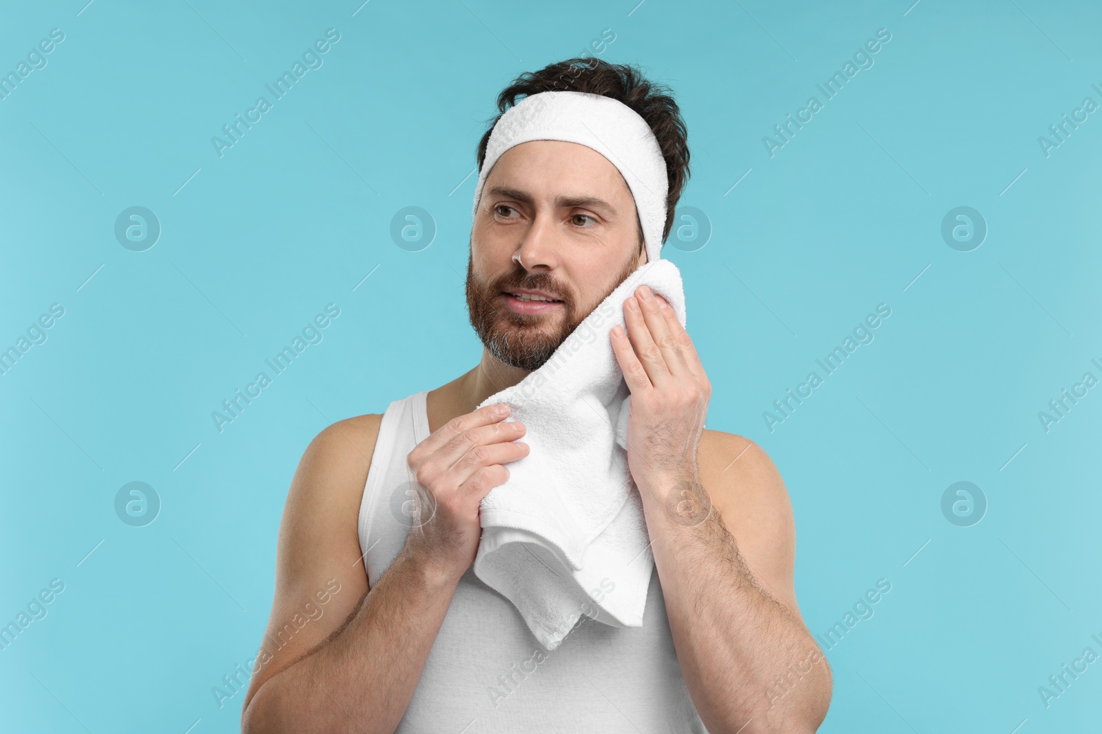 Photo of Washing face. Man with headband and towel on light blue background