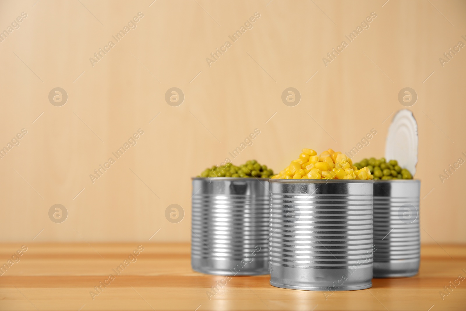 Photo of Open tin cans with conserved vegetables on wooden table. Space for text