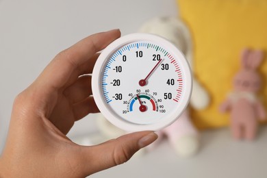 Photo of Woman holding round hygrometer with thermometer on blurred background, closeup
