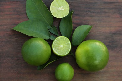 Photo of Whole and cut fresh ripe limes with green leaf on wooden table, flat lay