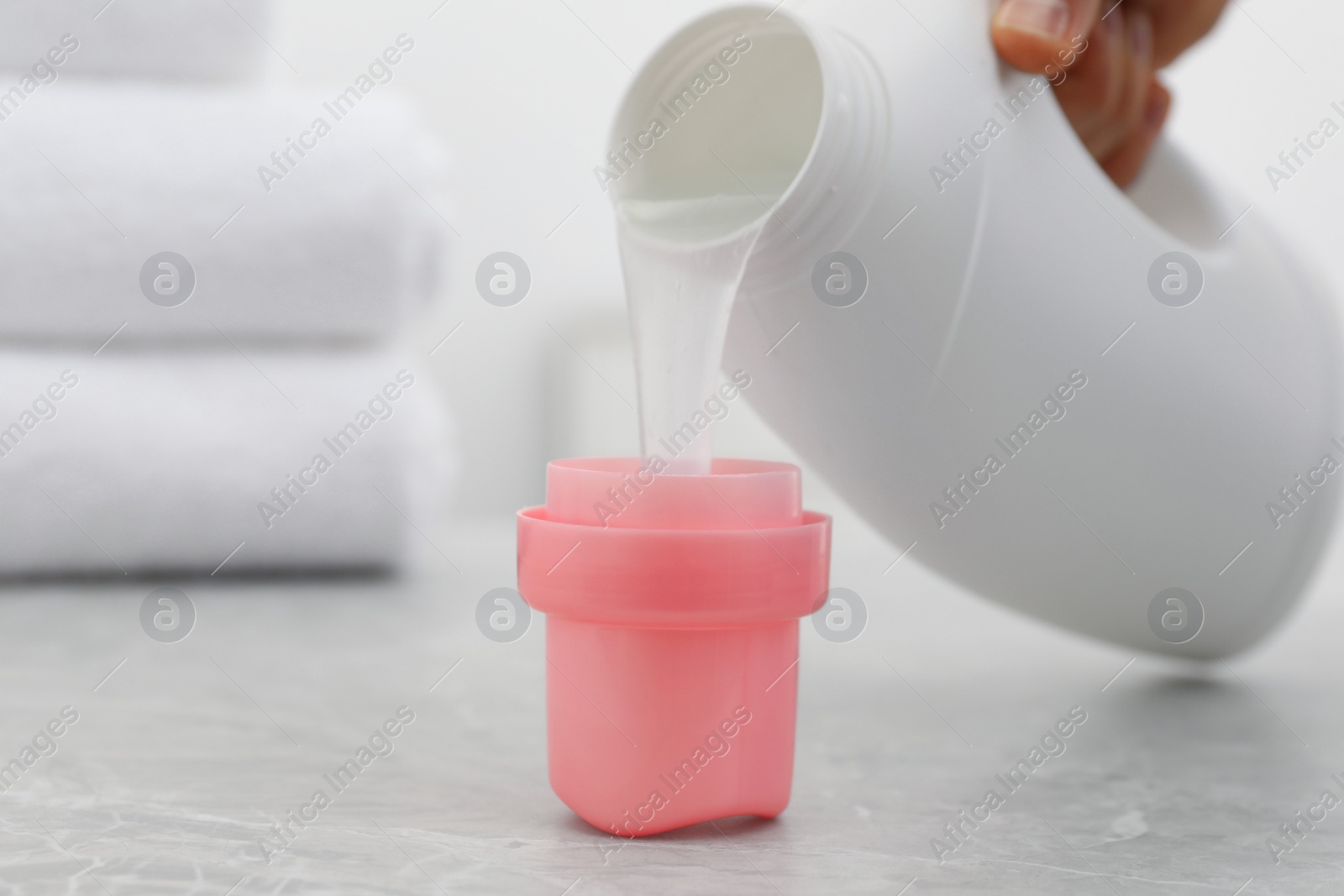 Photo of Woman pouring laundry detergent from bottle into cap at light grey marble table, closeup