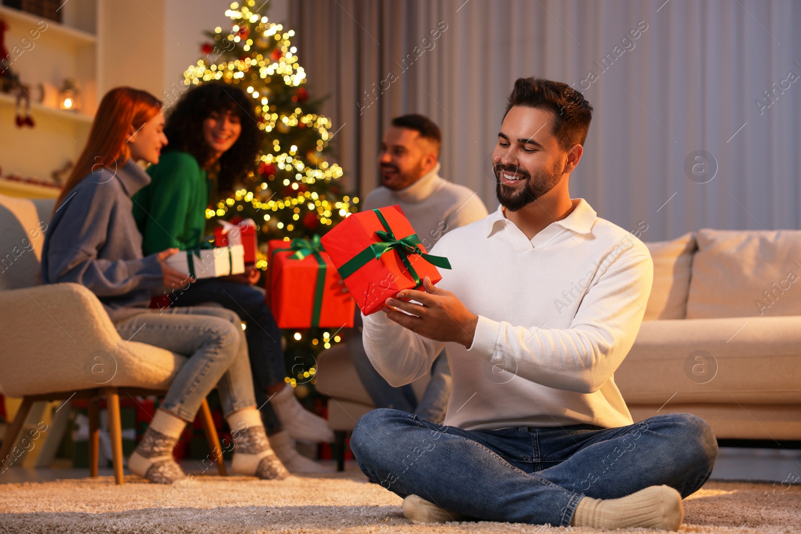 Photo of Christmas celebration in circle of friends. Happy young man with gift box at home, selective focus