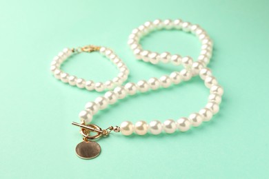 Photo of Elegant pearl necklace and bracelet on turquoise background, closeup