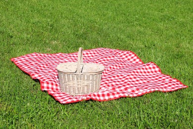 Picnic basket with checkered tablecloth on green grass outdoors