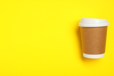 Takeaway paper coffee cup on yellow background, top view. Space for text