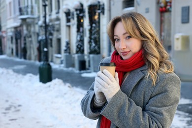 Photo of Portrait of charming woman with paper cup of coffee on city street. Space for text